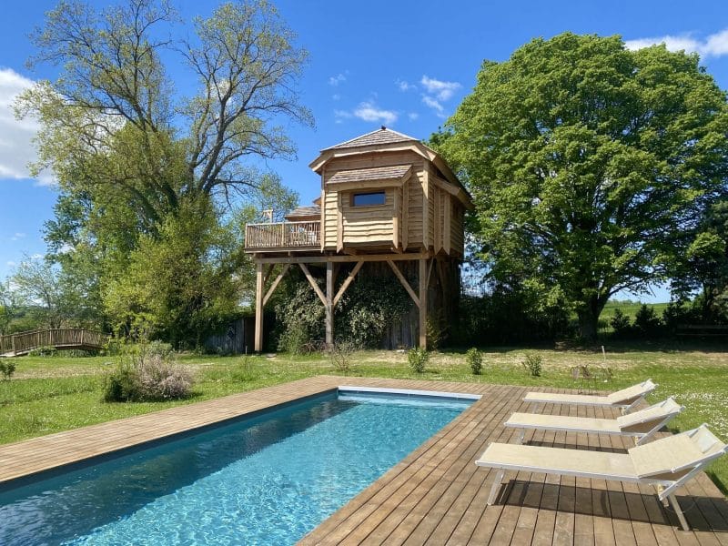 Cabane perchée avec piscine, entourée de verdure et ciel bleu. Détente assurée.