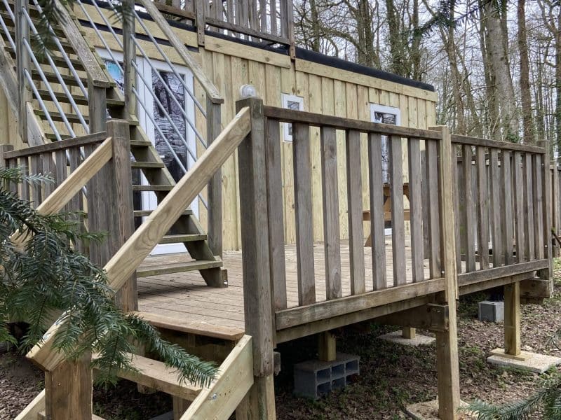 Cabane en bois sur pilotis, entourée darbres, avec une terrasse en bois accueillante.