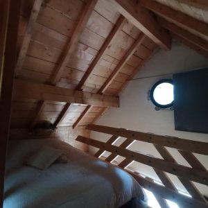 Chalet en bois avec lit douillet et fenêtre ronde, situé en Champagne-Ardenne.