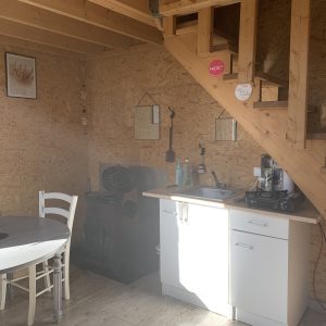 Cabane en bois avec cuisine équipée, poêle à bois et coin repas lumineux.