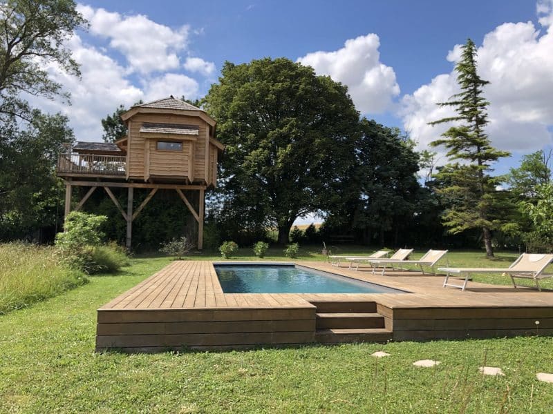 Cabane perchée avec piscine, entourée dun jardin verdoyant et darbres majestueux.