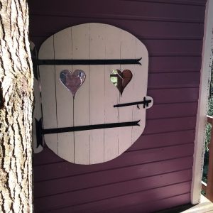 Cabane perchée avec une porte en bois décorée de cœurs, nichée dans les arbres.
