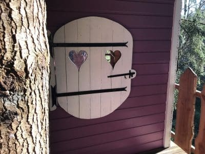 Cabane perchée avec une porte en bois décorée de cœurs, nichée dans les arbres.