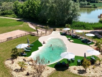 Hébergement insolite avec piscine naturelle, transats et parasols au milieu d'un cadre verdoyant.
