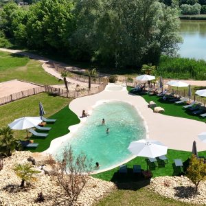 Hébergement insolite avec piscine naturelle, transats et parasols au milieu d'un cadre verdoyant.