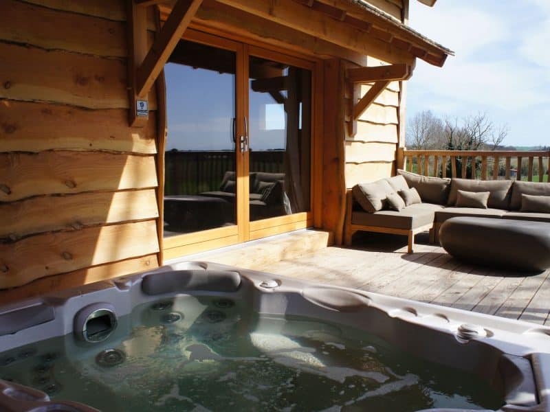 Chalet en bois avec jacuzzi sur la terrasse et vue sur la nature environnante.
