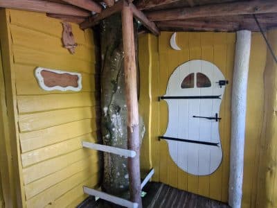 Cabane en bois colorée avec une porte blanche en forme de visage et un arbre à l'intérieur.