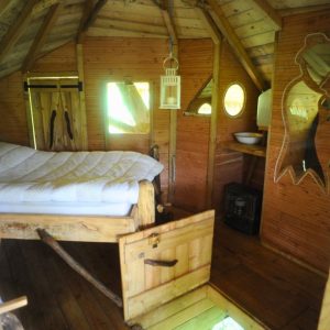 Cabane en bois avec lit douillet, fenêtres rondes et ambiance chaleureuse. Parfait pour se