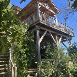 Cabane perchée en bois avec balcon, entourée de verdure à Midi-Pyrénées.