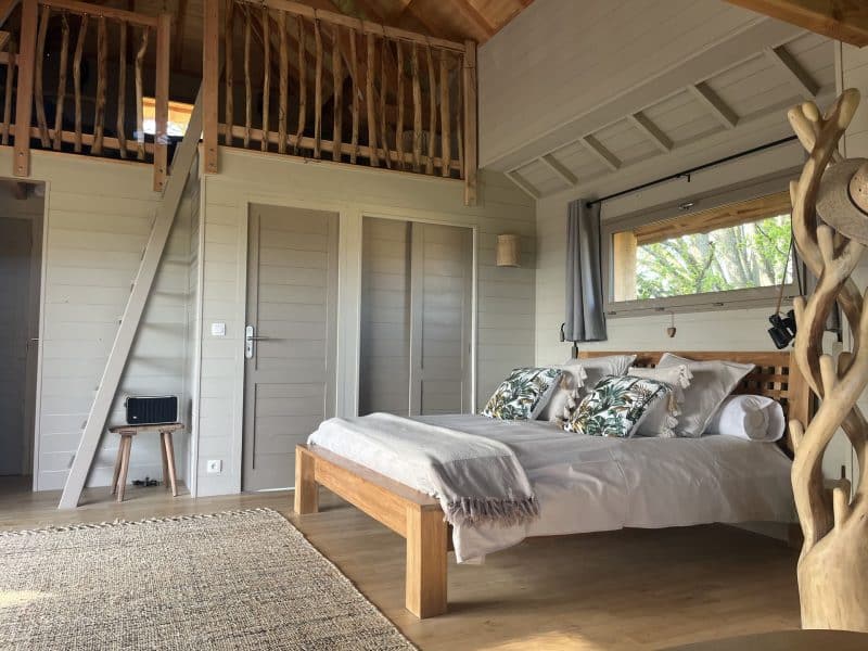 Chalet en bois avec lit douillet et décoration végétale, ambiance chaleureuse et lumineuse.