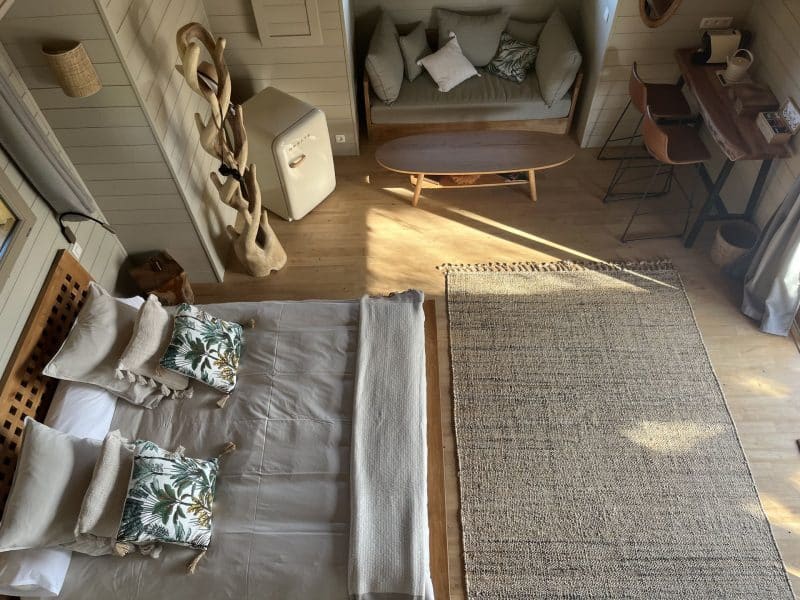Chalet moderne avec lit douillet, décor tropical et coin salon lumineux.