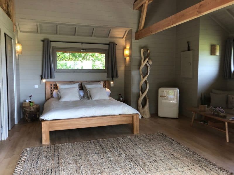 Chalet moderne avec lit en bois, décor chaleureux et vue sur la nature.