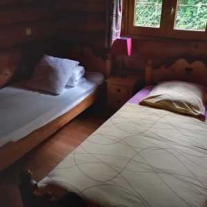 Chalet en bois avec deux lits simples, lumière douce et vue sur la nature.
