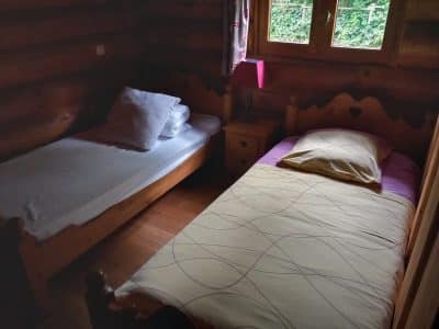 Chalet en bois avec deux lits simples, lumière douce et vue sur la nature.