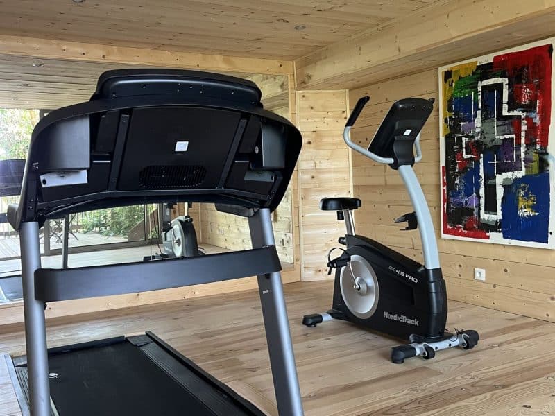 Salle de sport dans un chalet en bois, avec tapis de course et vélo dappartement.