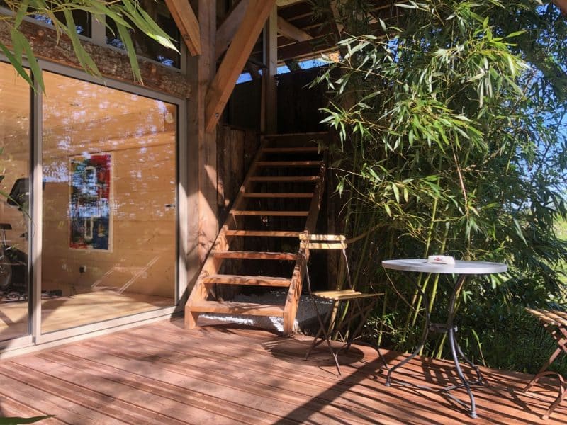 Cabane en bois sur pilotis, avec terrasse et escalier en bois entouré de bambous.