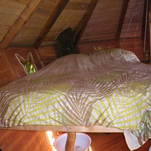 Cabane en bois avec un lit douillet, décoré de motifs végétaux et ambiance chaleureuse.
