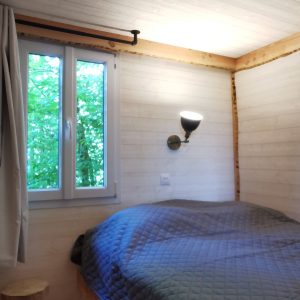 Chalet cosy en bois avec lit douillet et vue sur la nature verdoyante.