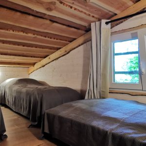 Chalet cosy avec lits simples, poutres apparentes et vue sur la nature à travers la fenêtre.