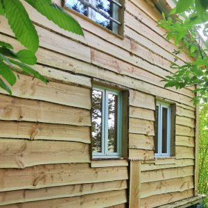 Cabane en bois au milieu de la verdure, avec des fenêtres encadrées de bois naturel.