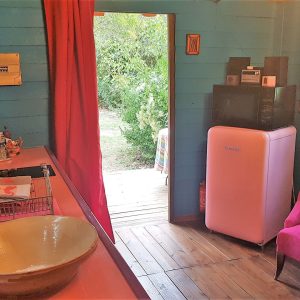 Charmante cabane colorée avec cuisine équipée et frigo rétro, ouverte sur la nature.