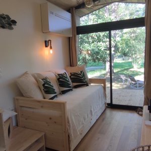 Chalet moderne avec lit en bois, grandes baies vitrées et vue sur la nature verdoyante.