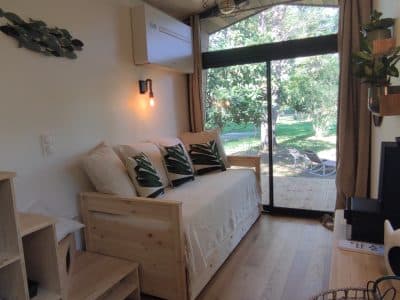 Chalet moderne avec lit en bois, grandes baies vitrées et vue sur la nature verdoyante.