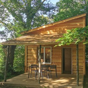 Charmante cabane en bois avec terrasse, nichée sous de grands arbres verdoyants.