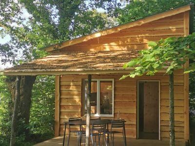 Charmante cabane en bois avec terrasse, nichée sous de grands arbres verdoyants.