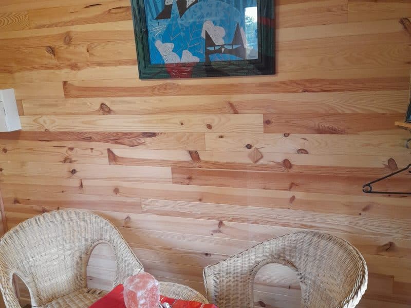 Chalet en bois chaleureux avec chaises en rotin et tableau coloré au mur.