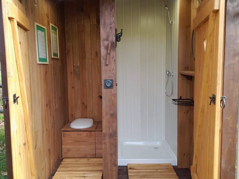 Cabane de jardin avec toilettes et douche en bois, ambiance naturelle et chaleureuse.