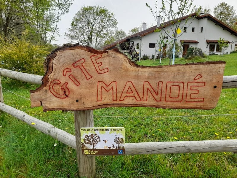 Gîte Manoé, charmant hébergement avec un panneau en bois dans un cadre verdoyant.