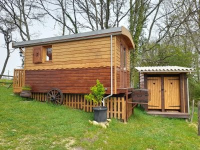 Charmante roulotte en bois surélevée, entourée de verdure, avec toilettes séparées en bois.