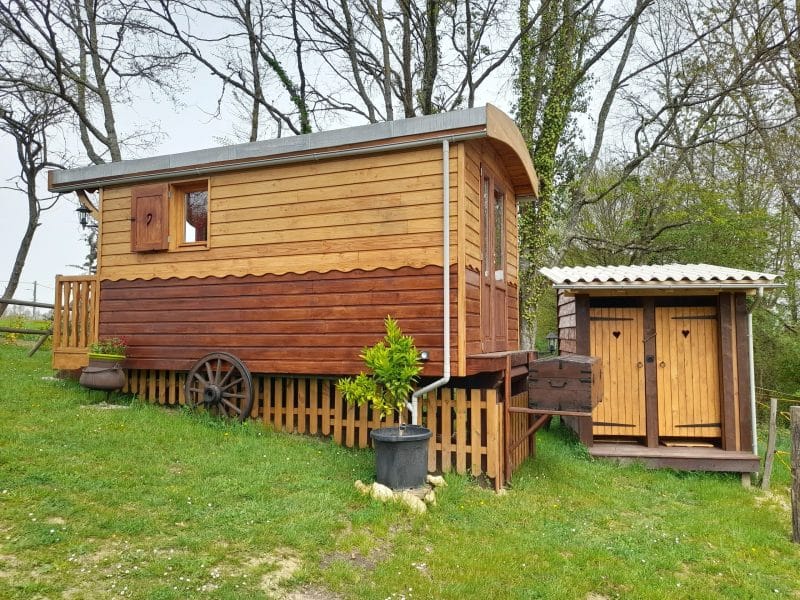 Charmante roulotte en bois surélevée, entourée de verdure et de cabanons en bois.