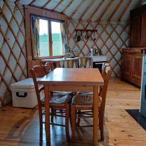 Intérieur d'une yourte chaleureuse, avec table en bois, chaises et cuisine équipée.