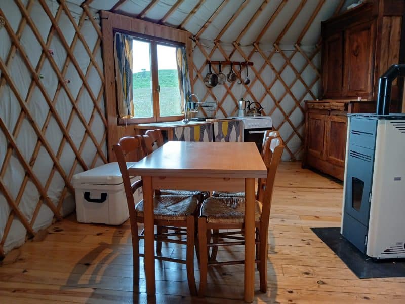 Yourte chaleureuse avec un intérieur en bois, table et cuisine équipée.