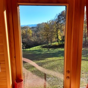 Vue panoramique depuis une cabane en bois, entourée de verdure et de collines.