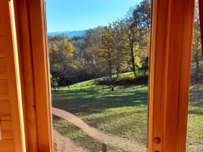 Vue panoramique depuis une cabane en bois, entourée de verdure et de collines.