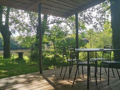 Terrasse en bois d'un chalet au bord de l'eau, entourée d'arbres verdoyants.
