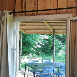 Vue sur une terrasse en bois depuis un chalet en bois, avec des chaises bleues et verdure