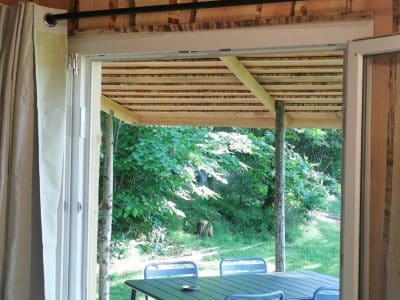 Vue sur une terrasse en bois depuis un chalet en bois, avec des chaises bleues et verdure