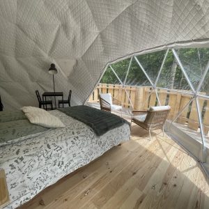 Dôme géodésique lumineux avec vue sur la nature, lit douillet et coin salon.