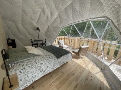 Dôme géodésique lumineux avec vue sur la nature, lit douillet et coin salon.