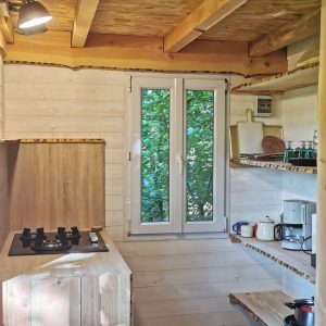 Intérieur d'une cabane en bois, avec cuisine équipée et lumière naturelle. Ambiance chaleureuse.