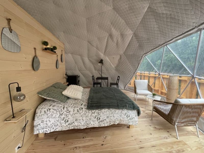 Dôme géodésique avec lit douillet, décor bois et vue sur la nature.