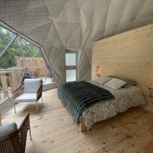 Dôme géodésique avec intérieur en bois, lit douillet et vue sur la nature.