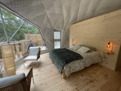 Dôme géodésique avec intérieur en bois, lit douillet et vue sur la nature.