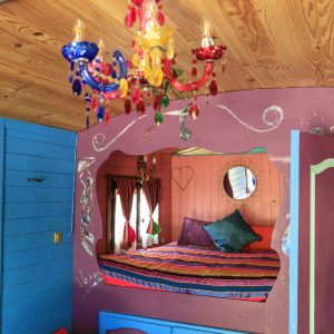 Chambre colorée dans un hébergement insolite, avec un lustre en verre et un lit douillet.