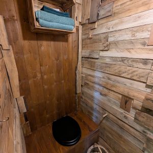 Toilettes en bois rustique, décorées de planches et de plantes, offrant une ambiance chaleureuse.