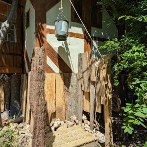 Cabane en bois rustique, avec un seau suspendu et des matériaux naturels environnants.